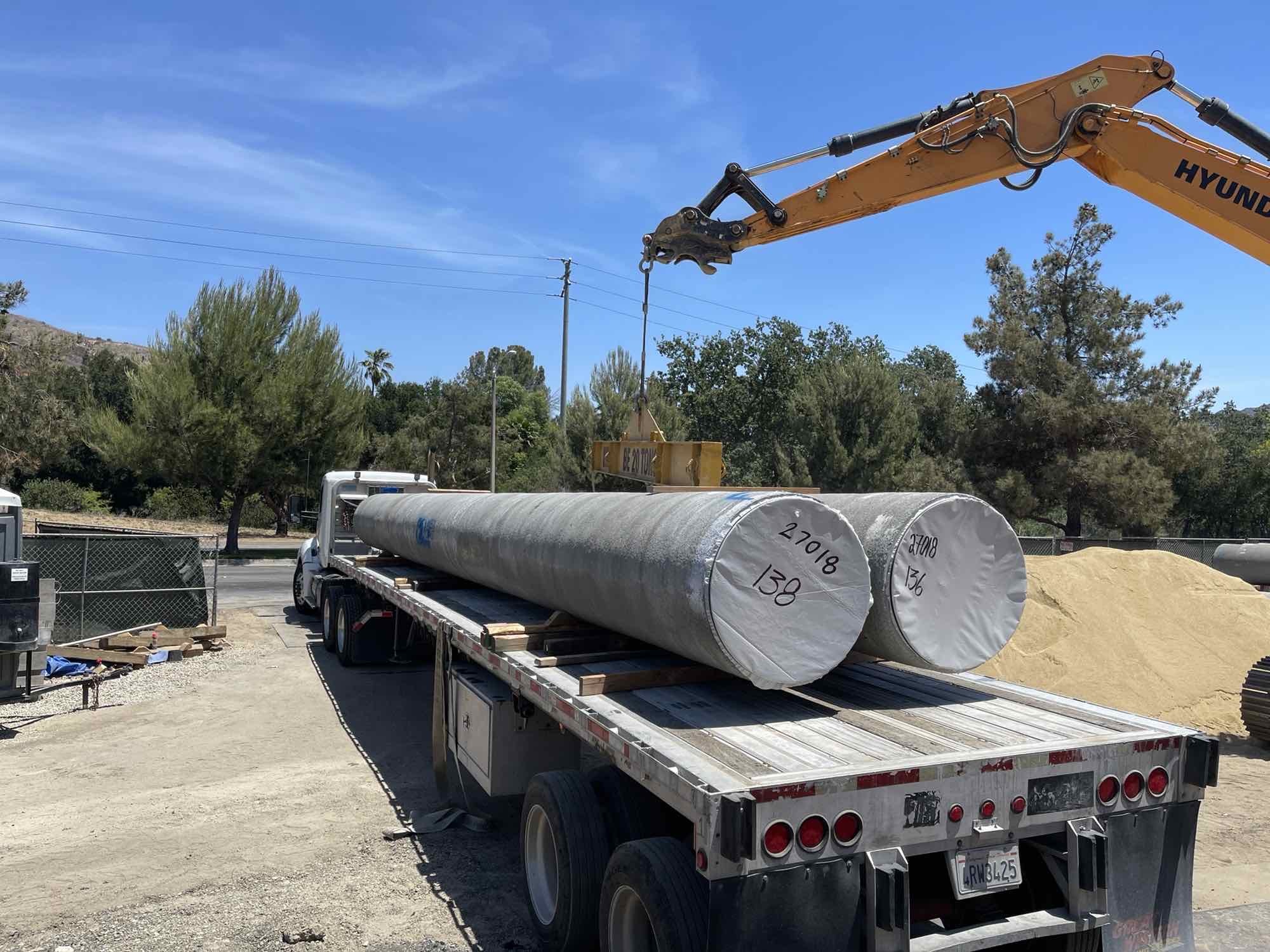 Large construction equipment removing concrete water mains off large flat bed semi-truck